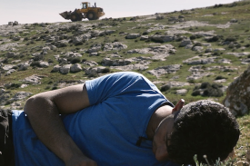 a bulldozer on top of a hill with a young man lying in a field